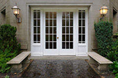 Elegant stone walkway bordered by stone benches leading to a double glass paned front door with two