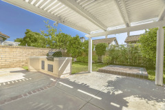 Concrete Patio Of A Home With Barbecue Grill And White Wooden Pergola