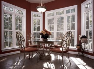 A dining room furnished with a table and chairs surrounding by beautiful, large windows.