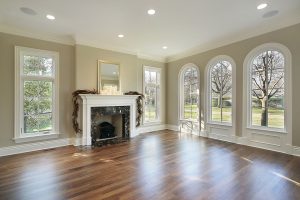 A large well-lit room with wood floors, a fireplace, and new windows. 